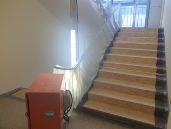 Treppenraum im Baugeschehen. Die Treppe ist mit Schutzmaterialien abgedeckt. Das Geländer ist mit einer Folie eingehüllt.