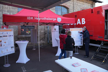 Bei einem Pavillon wird durch einen IBK-Mitarbeiter ein Poster für 2 Personen erklärt. Im Hintergrund ist das MOBLAB zu sehen.