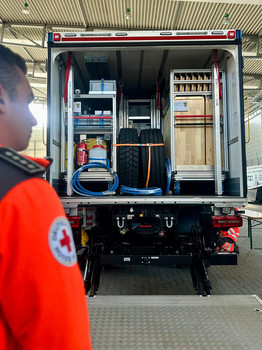 Person steht vor geöffneter LKW-Klappe. Im LKW sind Materialen verlastet.