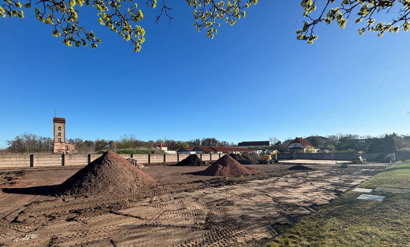 Sportplatz auf dem große Erdhaufen liegen und im Hintergrund Bagger arbeiten