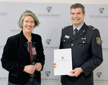 Innenministerin Zieschang (links stehend) übergibt dem Direktor rechts eine Ernennungsurkunde